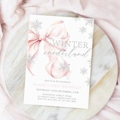 a white and pink winter wonderland birthday party card on a marble plate with snowflakes