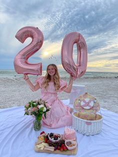 a woman in a pink dress holding up the number twenty two balloons on a beach