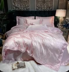 a bed with pink comforter and pillows in a room next to a lamp on the floor