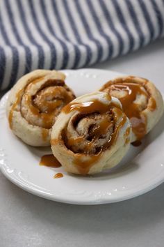 three cinnamon rolls on a white plate with caramel sauce