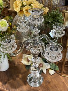 a glass candelabra sitting on top of a wooden table next to flowers