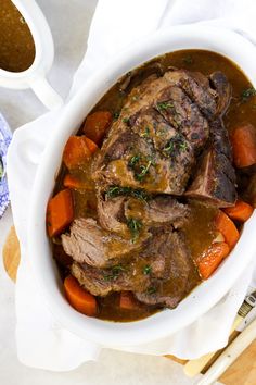 a white bowl filled with meat and carrots on top of a table next to a fork