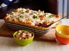 a casserole dish with pasta and meat in it on a cutting board next to two bowls