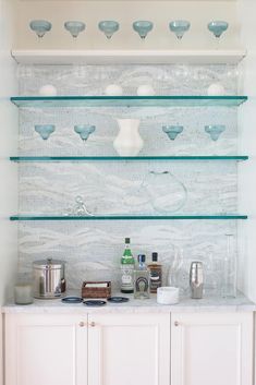 a kitchen counter with glass shelves above it and bottles on the top shelf, along with other items