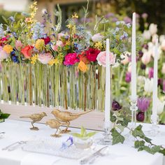 two birds are sitting on a table with flowers and candles