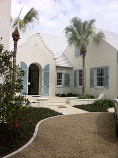 a car parked in front of a white house with blue shutters and palm trees