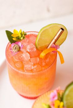 a close up of a drink in a glass on a plate with limes and flowers