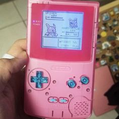 a person holding up a pink gameboy with an animal on it's screen