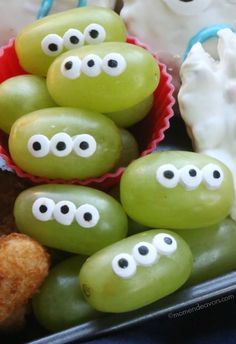 some green grapes with googly eyes on them and other food items in the background