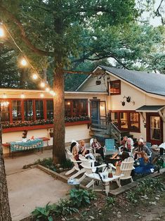 a group of people sitting around a table in front of a house with lights on