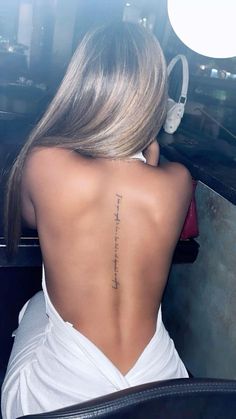 the back of a woman's neck with a tattoo on her lower back and words written in cursive writing