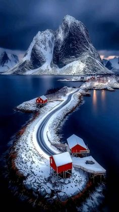 an island in the middle of water with snow on it and two red houses near by