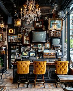 two yellow chairs sitting in front of a bar with pictures on the wall and chandelier