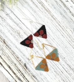 three triangle shaped beaded earrings sitting on top of a wooden table next to flowers