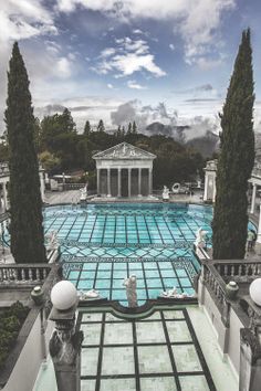 an outdoor swimming pool surrounded by trees and statues in front of a building with columns