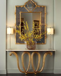 an ornate console table with a mirror above it and flowers in a vase on top