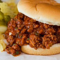 a close up of a sandwich and some food on a paper wrapper with broccoli in the background