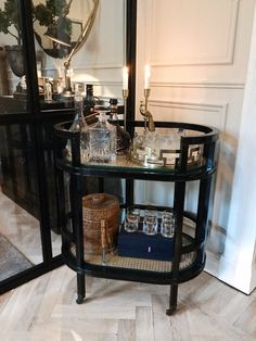 a glass table with bottles and glasses on it in front of a mirror, next to a candle