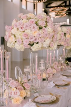 the table is set with pink and white flowers in tall vases, candles and plates