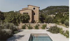 an outdoor swimming pool in front of a stone building with trees and bushes around it