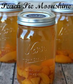 three mason jars filled with peaches sitting on top of a wooden table