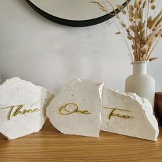 three pieces of white rock with gold lettering on them sitting on a table next to a vase