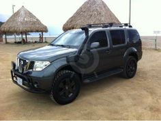 a grey suv parked in front of some straw umbrellas and thatched roof huts