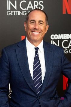 a man in a suit and tie smiles for the camera while standing on a red carpet