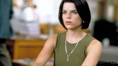 a woman sitting at a table with a necklace on her neck and looking off to the side