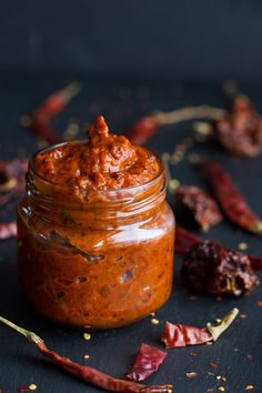 a jar filled with chili paste sitting on top of a table next to dried peppers