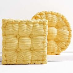 two yellow cushions sitting next to each other on a white surface with one cushion made out of woven material