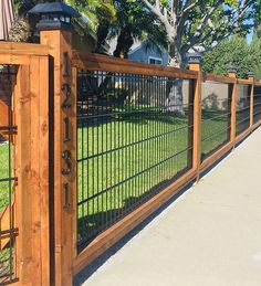 a wooden fence with black iron fencing on the top and bottom, next to a sidewalk