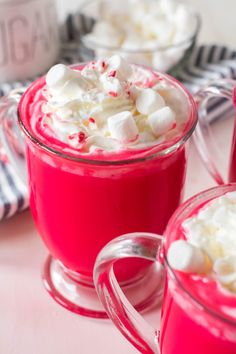 two mugs filled with hot chocolate and marshmallows on top of a table