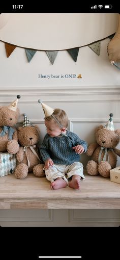 a little boy sitting on top of a wooden table surrounded by teddy bears wearing party hats