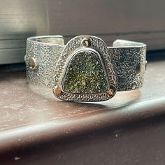 A beautiful custom hand made bracelet cuff in sterling silver and 14kt yellow gold bezel set with a unique shield shape rainbow pyrite druzy with flecks of various colors in peach, green, blue, gold, purple and turquoise.  The artist Monroe Jackson award winning jeweler custom made this bracelet by hand and fits a size 6 to 8.5" wrist.  The width across the top is 1.8" at the widest point.  The inscription reads pyrite, Monroe Jackson, SS-14k HEO.  The weight is 53.93 grams.  A beautiful one of Bezel Cuff Bracelet, Unique Gold Sterling Silver Cuff Bracelet, Luxury Silver Jewelry With Natural Inclusions, Valley View, Bracelet Cuff, Creative Jewelry, Druzy, Blue Gold, Cuff Bracelet