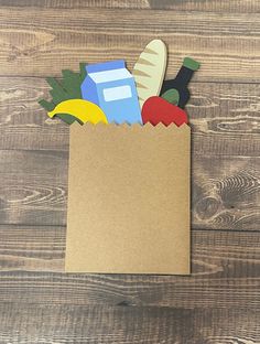 a brown paper bag filled with different types of cut out items on top of a wooden table