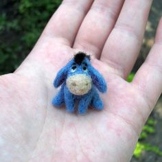 a small blue stuffed animal sitting on someone's palm in front of some trees