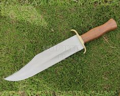 a large knife laying on top of a green grass covered field next to a wooden handle