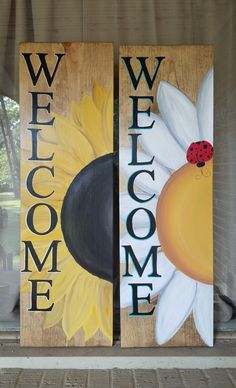 two wooden signs with the words welcome and a sunflower painted on them, sitting in front of a window