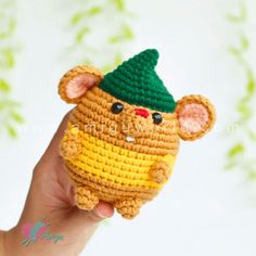 a hand holding a small crocheted toy with a green hat on it's head