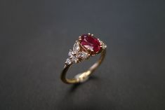 a close up of a ring with a red stone and two white diamonds on it