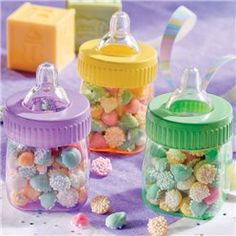 three baby bottles filled with colorful candies on top of a purple cloth covered table