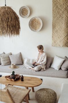 a woman sitting on top of a couch next to a coffee table and wicker baskets