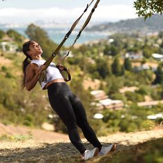 a woman holding onto a pole while standing on top of a hill with trees in the background