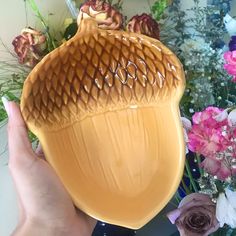 a hand holding a yellow vase with flowers in the background