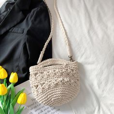 a crocheted purse sitting on top of a bed next to yellow tulips