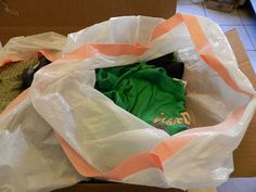 an open white plastic bag on top of a cardboard box filled with clothes and other items