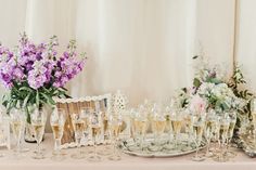 a table topped with lots of glasses filled with champagne next to vases and flowers