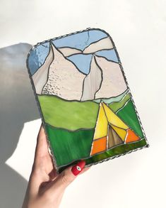 a hand holding up a small stained glass box with mountains and tents in the background