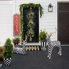 two deer statues sitting in front of a black and white house decorated with christmas greenery